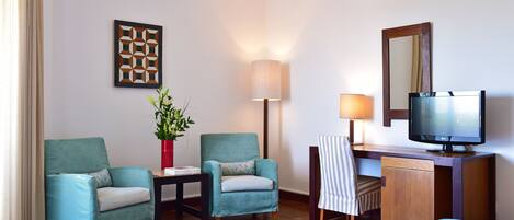 Een hotelkamer met twee fauteuils, een bureau met een televisie, een lamp en een kunstwerk in een lijst aan de muur.