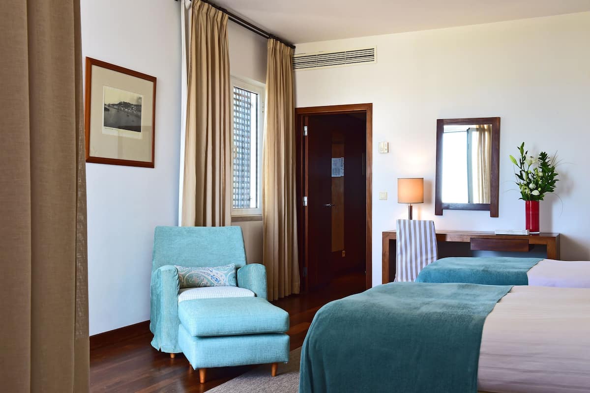 A hotel room with a bed, a chair, a desk, a lamp, a mirror, and a window with curtains.