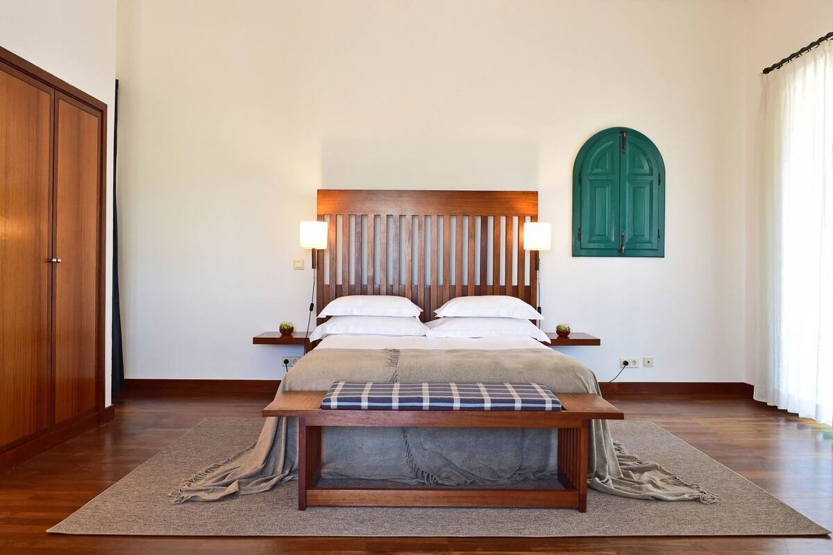 A bedroom with a wooden bed, bedside tables, a green door, and a large window.