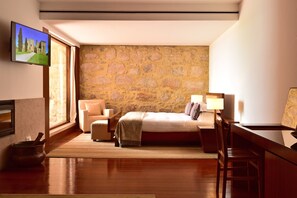 A bedroom with a stone wall, a bed, a desk, a chair, a TV, and a window. - Pousada Mosteiro Crato (Crato)