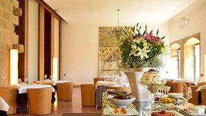 Un comedor con mesas dispuestas para una comida, un gran centro de mesa floral y un mural en la pared.