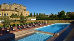 Una piscina con sillones de descanso y un castillo al fondo.