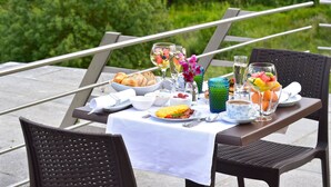 Mesa de comedor al aire libre con alimentos para el desayuno, como cruasanes, huevos y fruta.