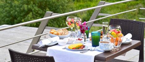 An outdoor dining table set with breakfast items, including croissants, eggs, and fruit.