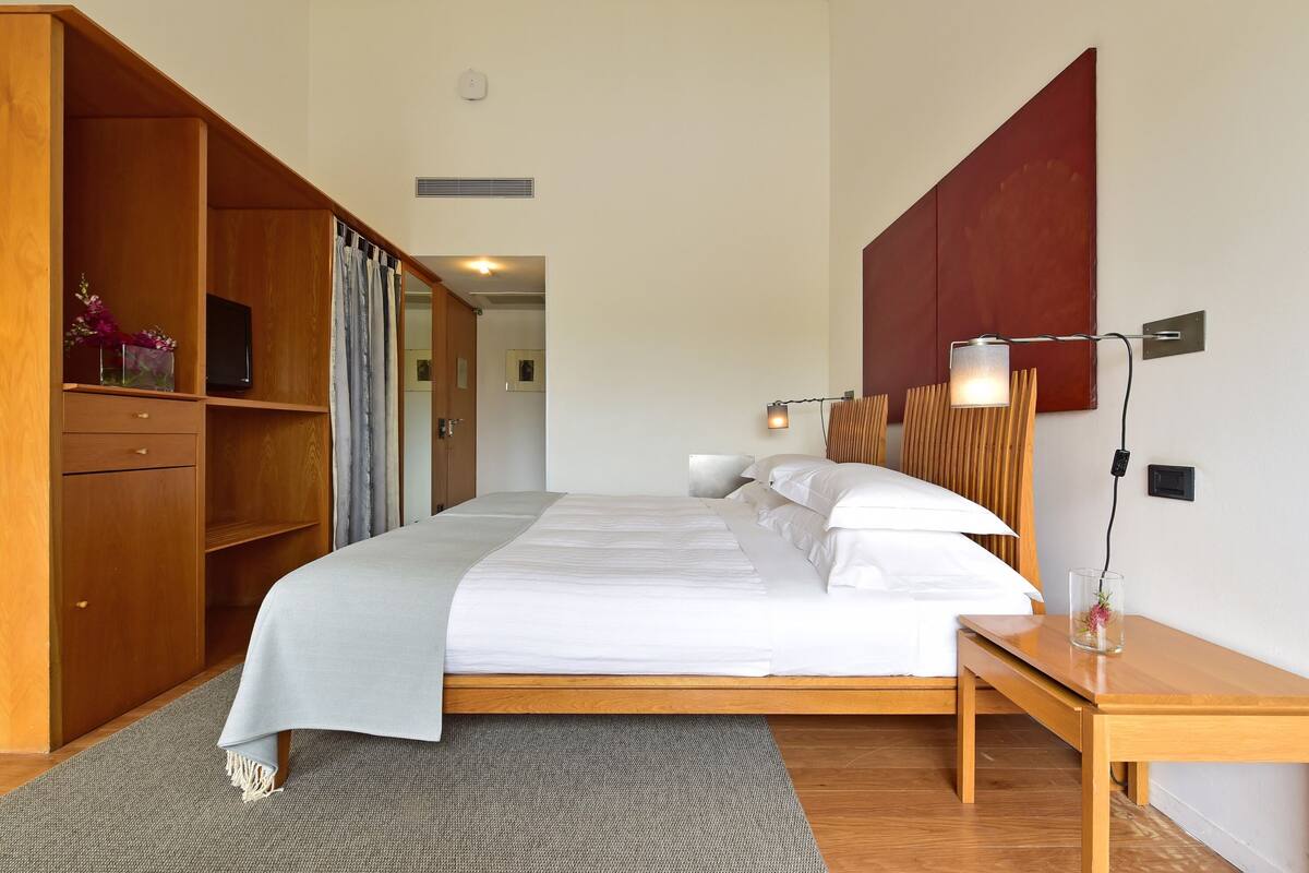 A neatly arranged bedroom with a bed, bedside table, lamp, and wooden wardrobe.