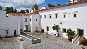 Un patio con piscina, edificios blancos y tejado de tejas rojas.