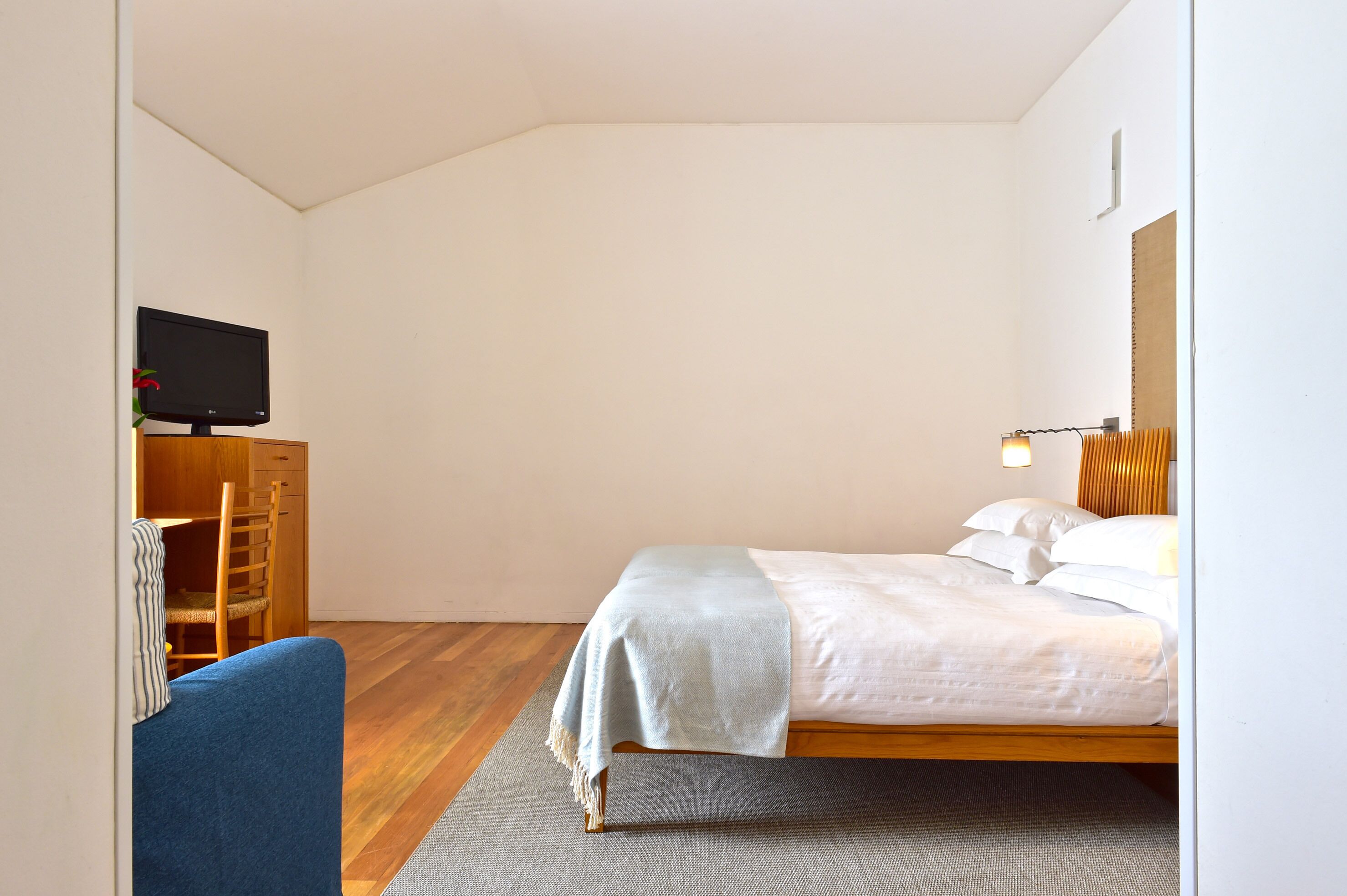 A bedroom with a bed, a desk with a computer, a chair, and a television on a stand.