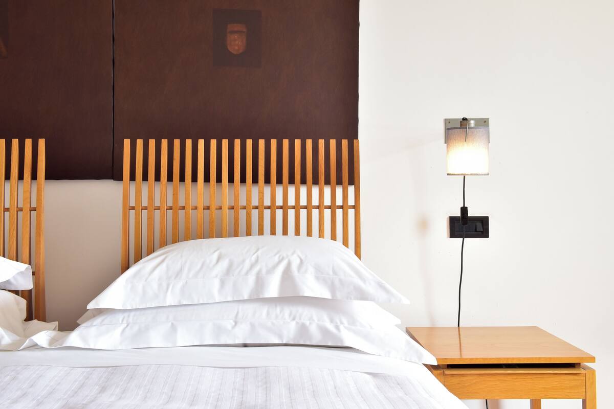 A neatly made bed with white linens, a wooden headboard, and a bedside table with a lamp.