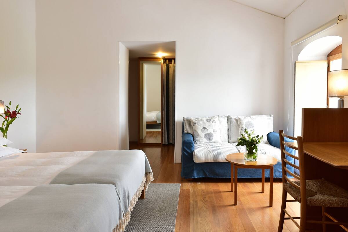 A hotel room with two beds, a sofa, a dining table, and a chair.
