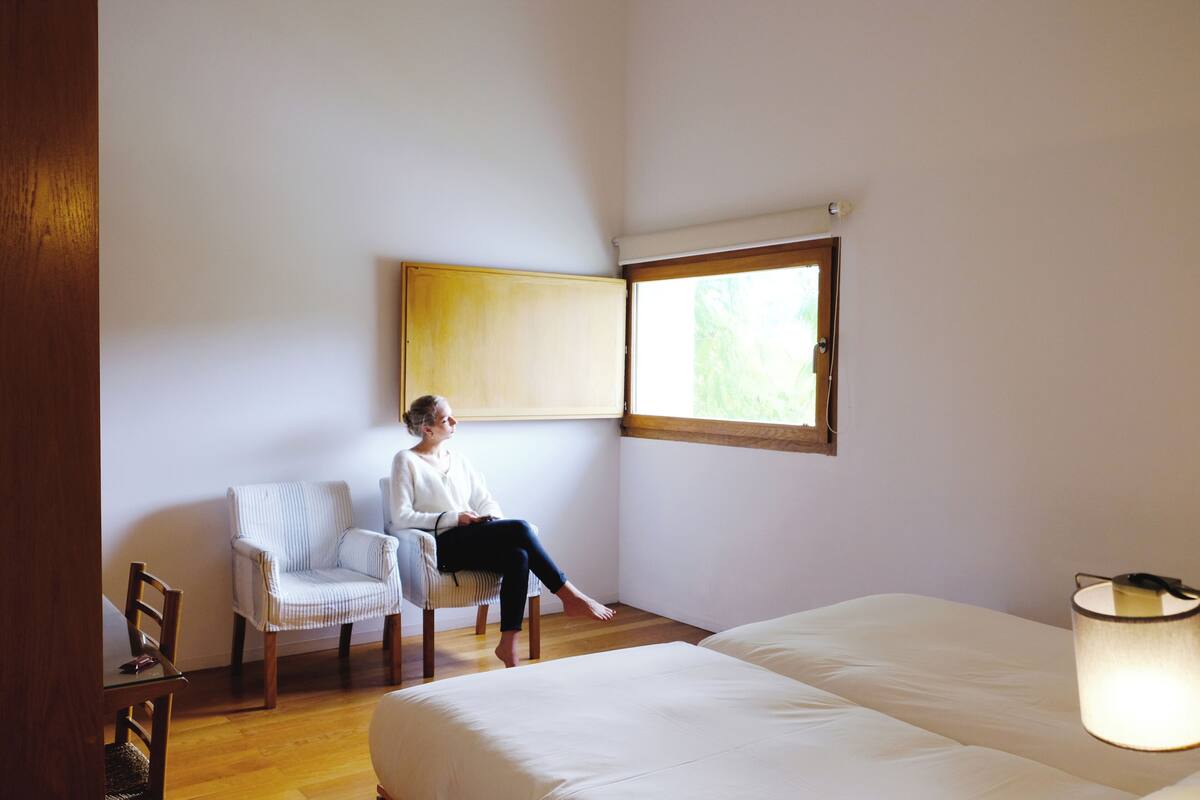 A room with a bed, a chair, a window, and a lamp.