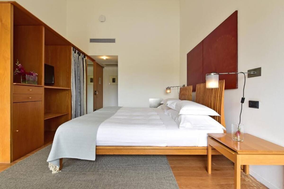 A modern hotel room with a large bed, wooden furniture, and a red accent wall.