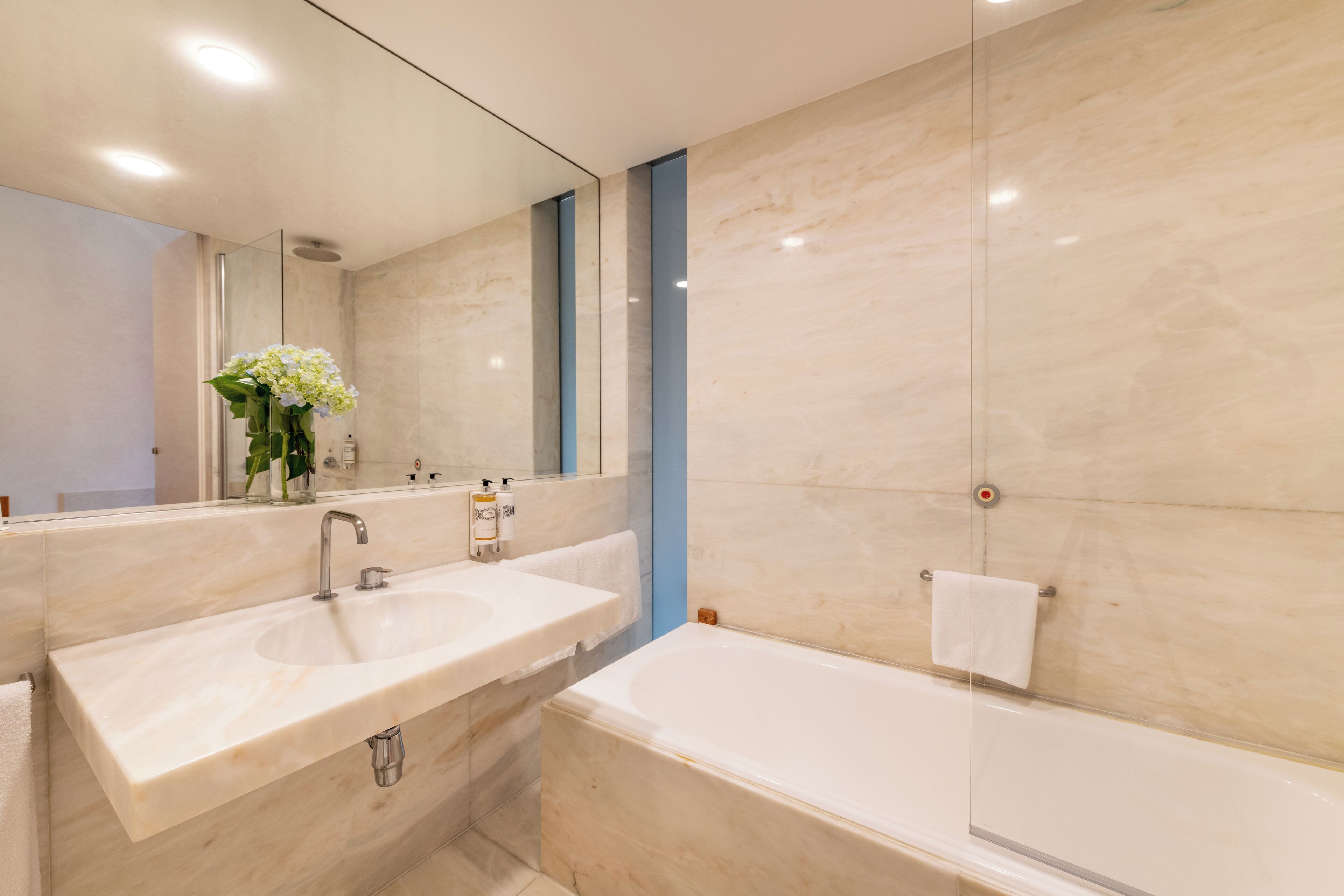 A modern bathroom with a large mirror, a sink, and a bathtub.