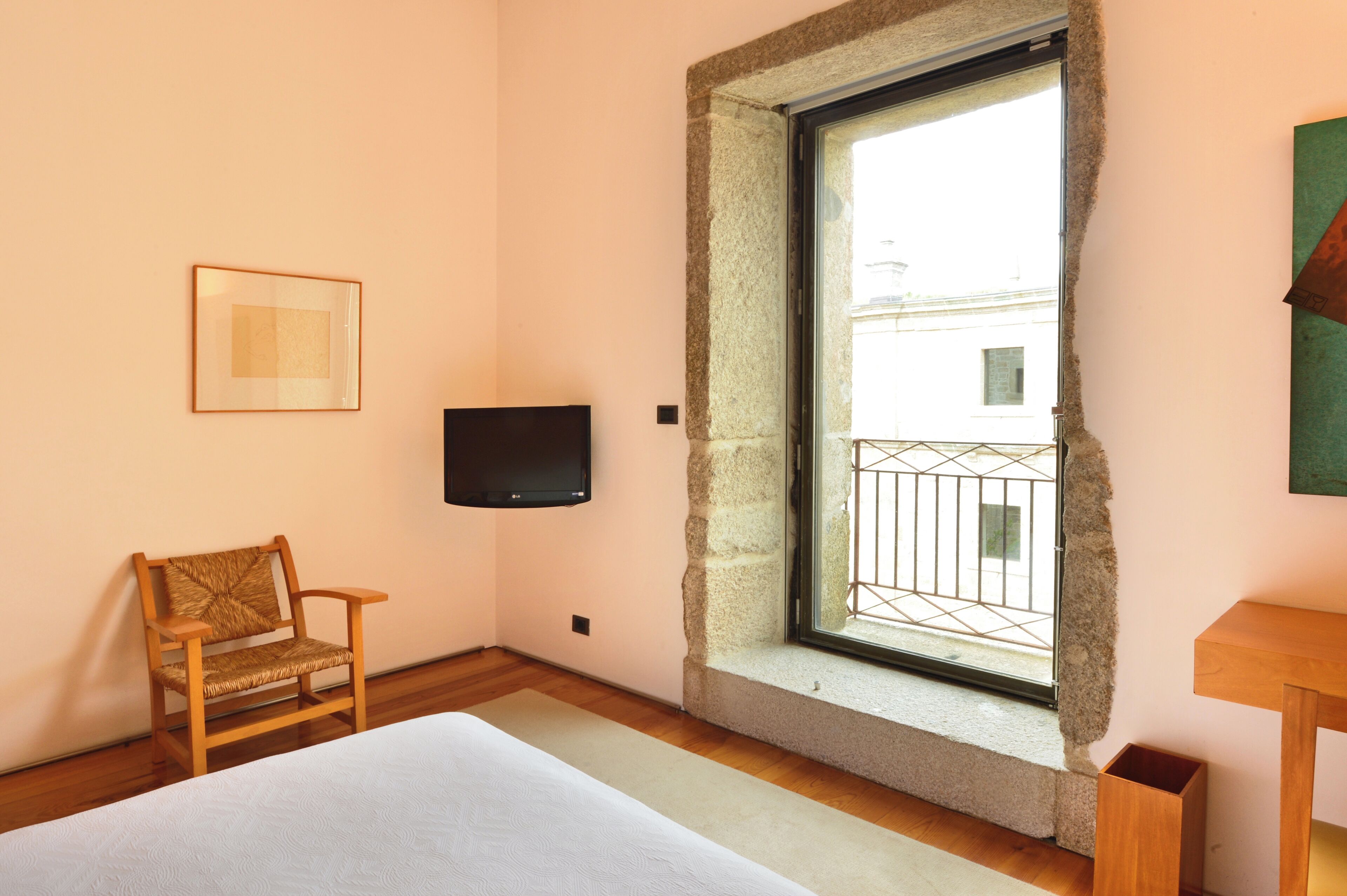 Een slaapkamer met een bed, een stoel, een televisie en een raam met uitzicht op gebouwen.