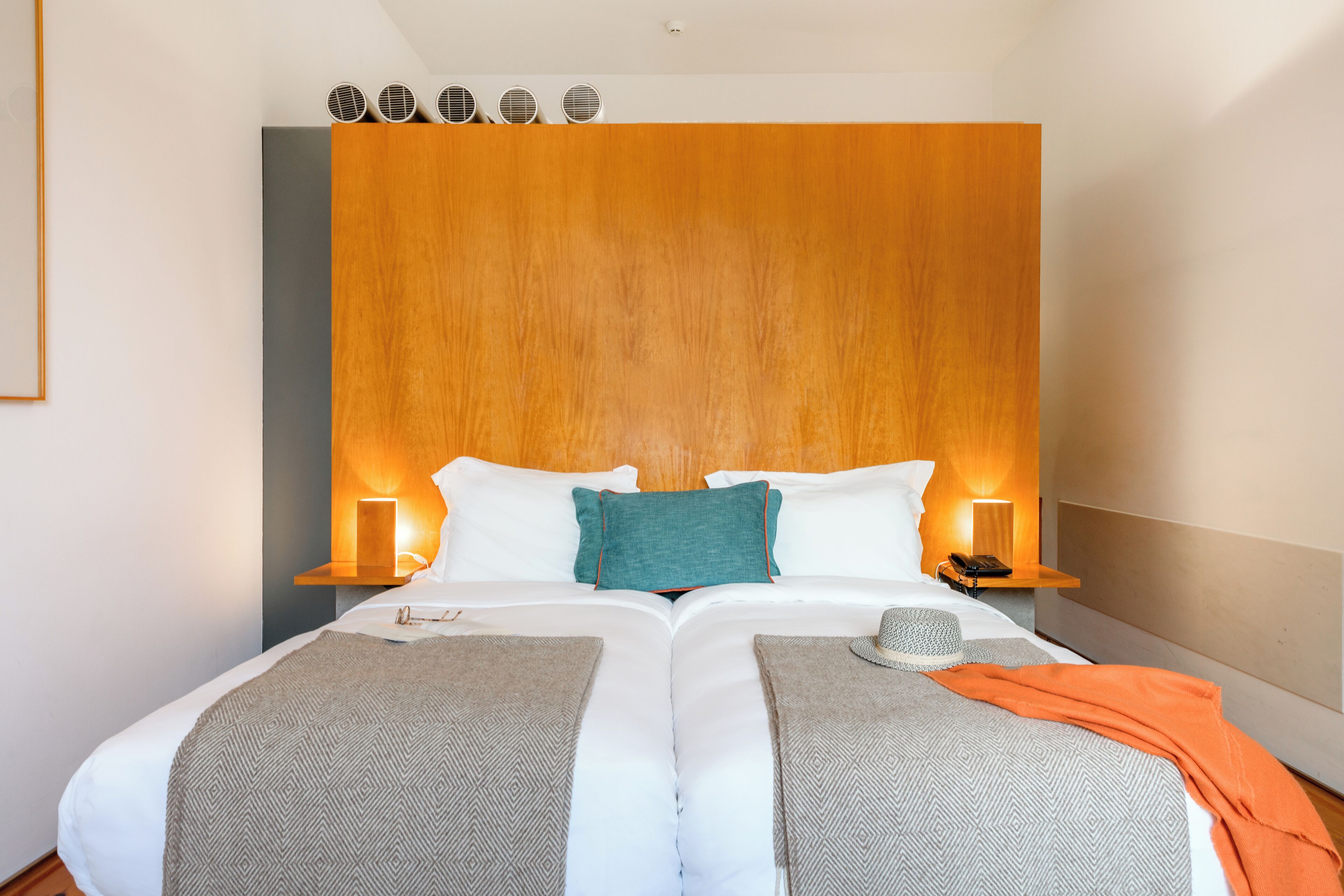 A double bed with two pillows, a wooden headboard, bedside lamps, and a hat on the bed.