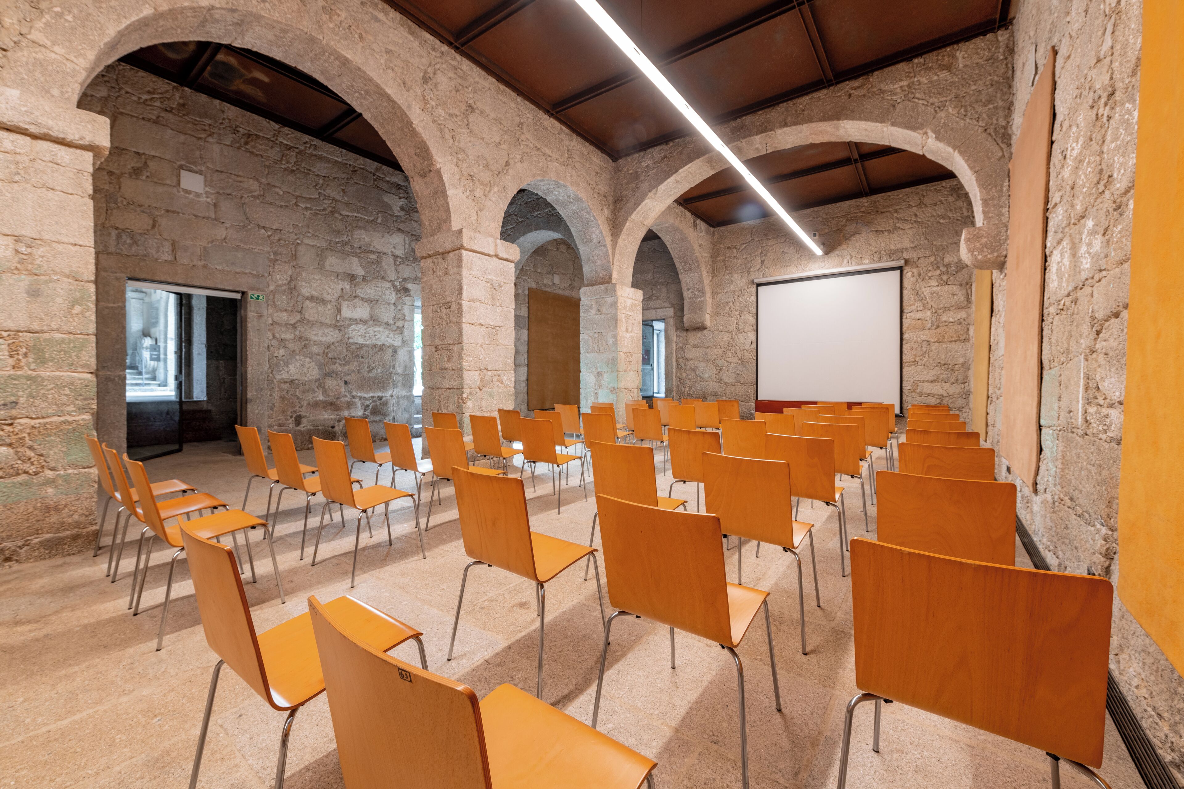 A lecture hall with stone arches, wooden chairs, and a whiteboard.