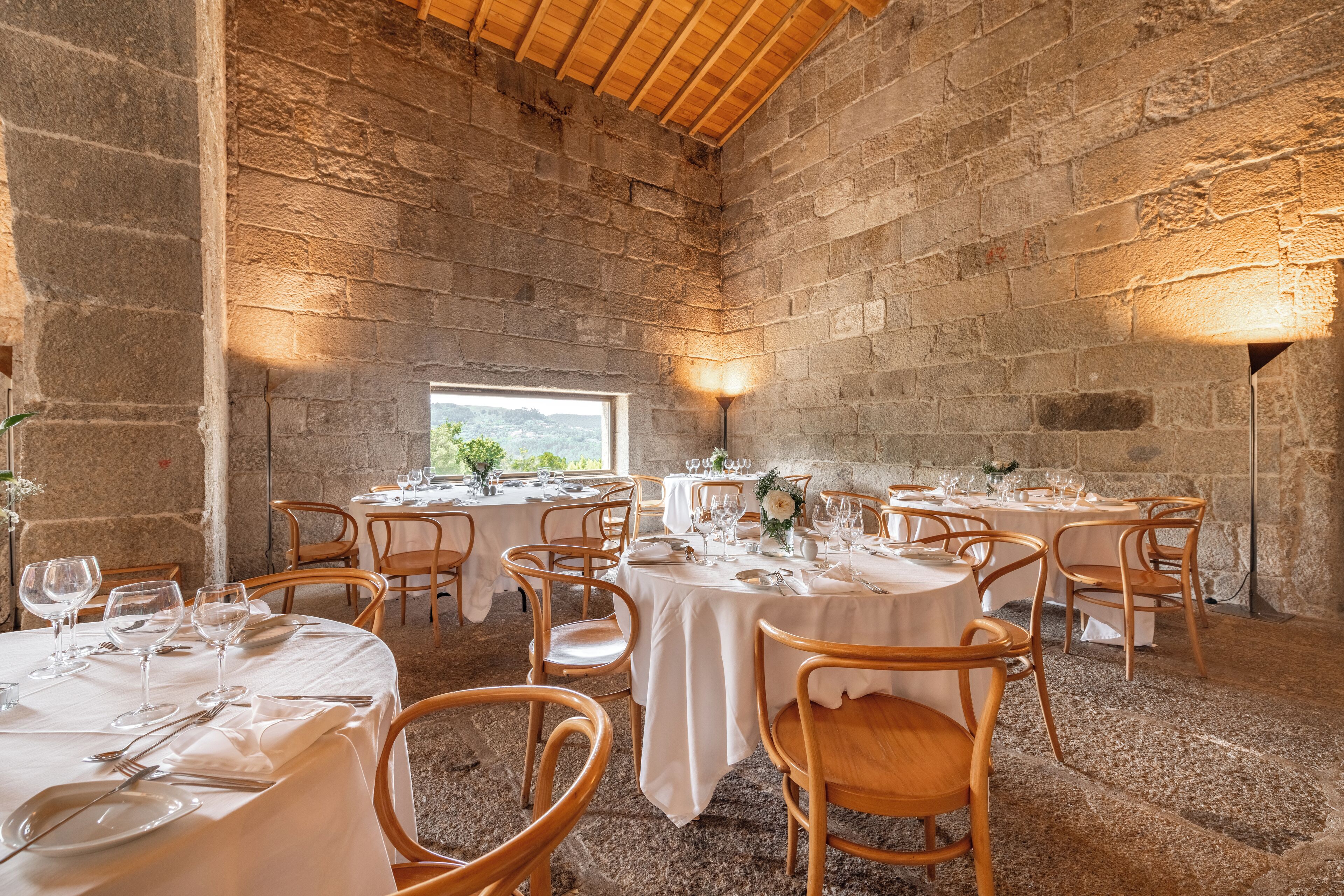 A rustic dining area with stone walls, round wooden tables, and white tablecloths.