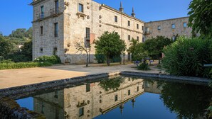 Un edificio histórico de piedra con un patio y un estanque reflectante.