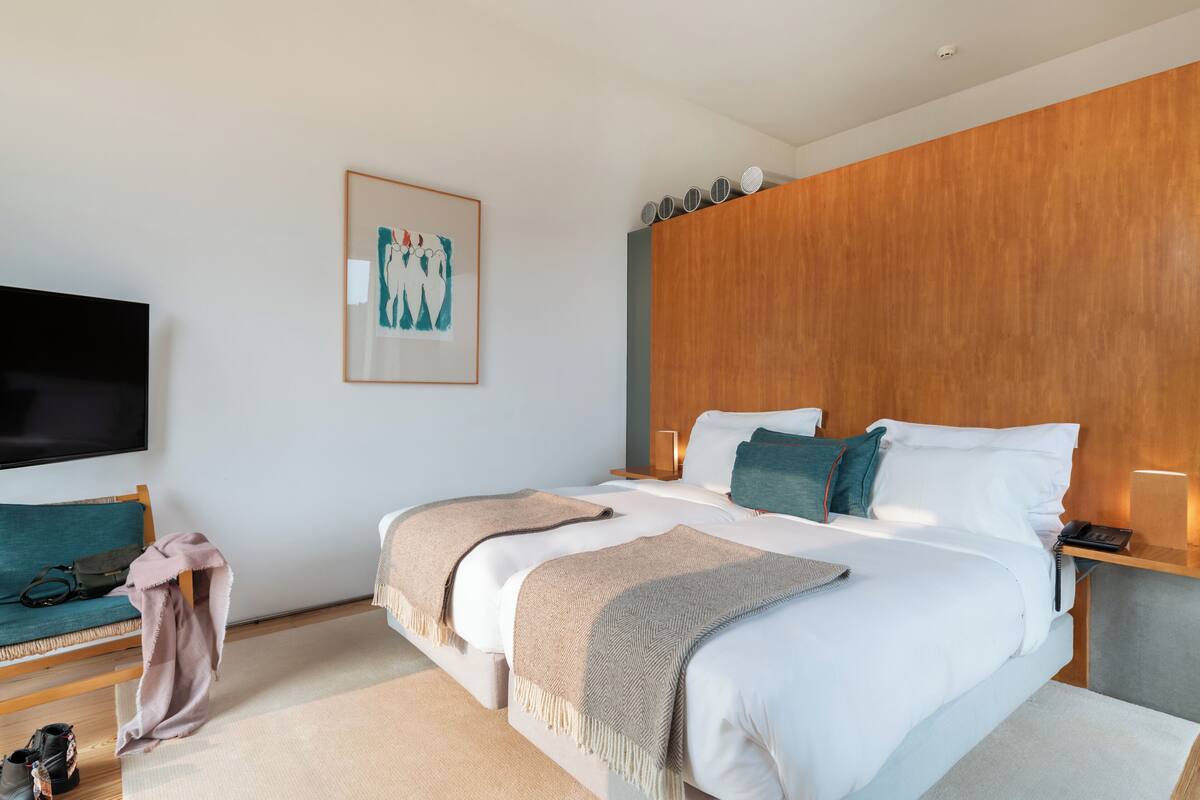 Una habitación de hotel moderna con una cama grande, un televisor de pantalla plana, un cabecero de madera y una obra de arte enmarcada en la pared.