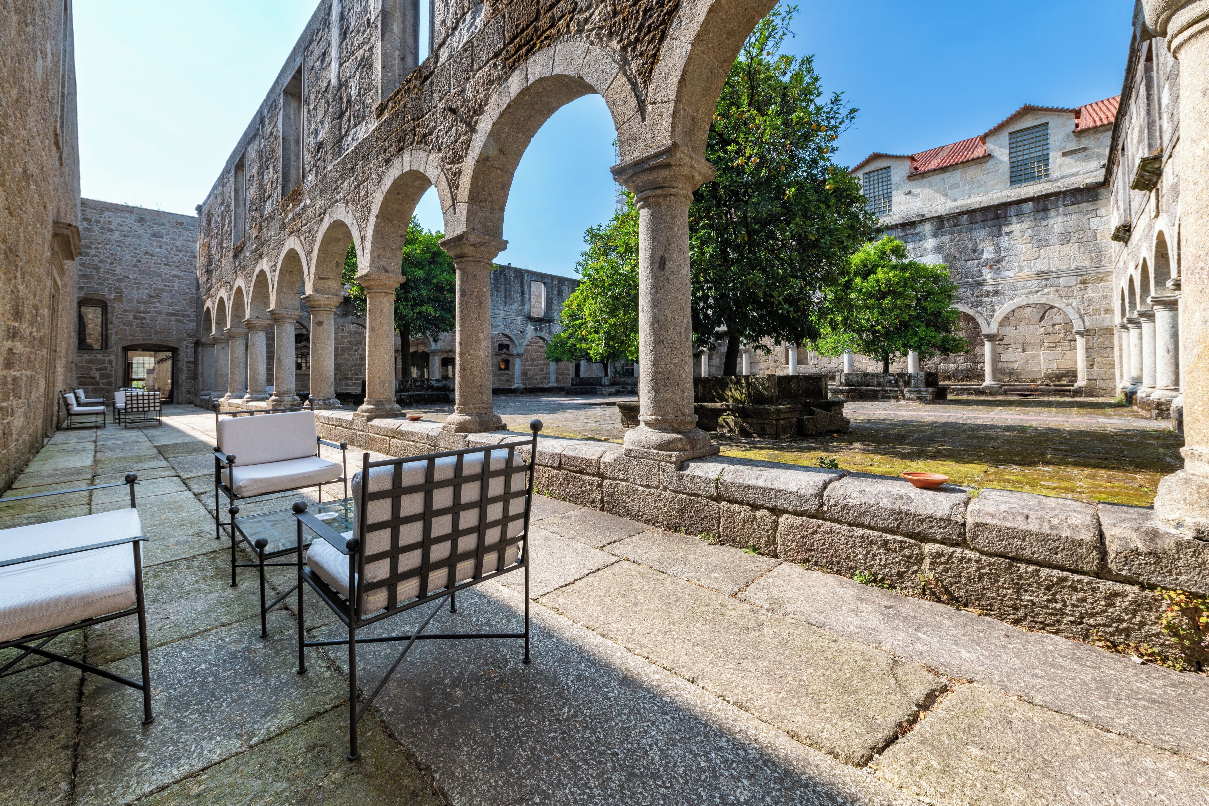 Un patio con bancos y mesas de piedra, arcos y una fuente.