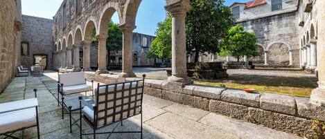 Un patio con bancos y mesas de piedra, arcos y una fuente.