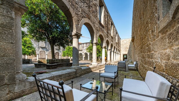 Un área de estar al aire libre con columnas de piedra, un árbol y vistas de un edificio histórico.