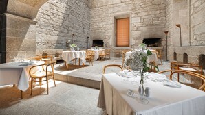 Comedor con paredes de piedra, mesas dispuestas para una comida, chimenea y luz natural.
