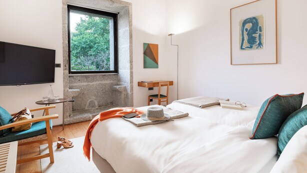 A modern bedroom with a large bed, a television, a stone wall, and artwork on the walls. - Pousada Mosteiro Amares (Amares)