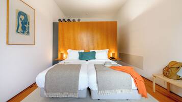 A double bed with a wooden headboard, two bedside tables with lamps, a framed artwork on the wall, and a bench with a bag on it.