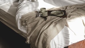 Una cama con sábanas blancas, una bandeja de madera con una taza y un platillo, y un plato decorativo.