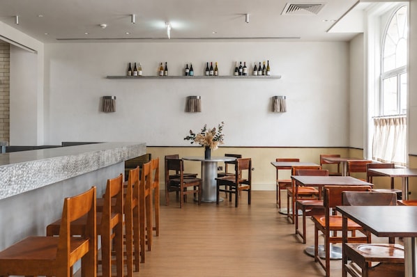 A restaurant with a bar area, wooden chairs, tables, and shelves with bottles. - Arthouse Hotel Glasgow (Glasgow)