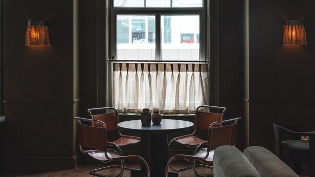 Una habitación con una mesa redonda, dos sillas, un sofá y una ventana con cortinas.