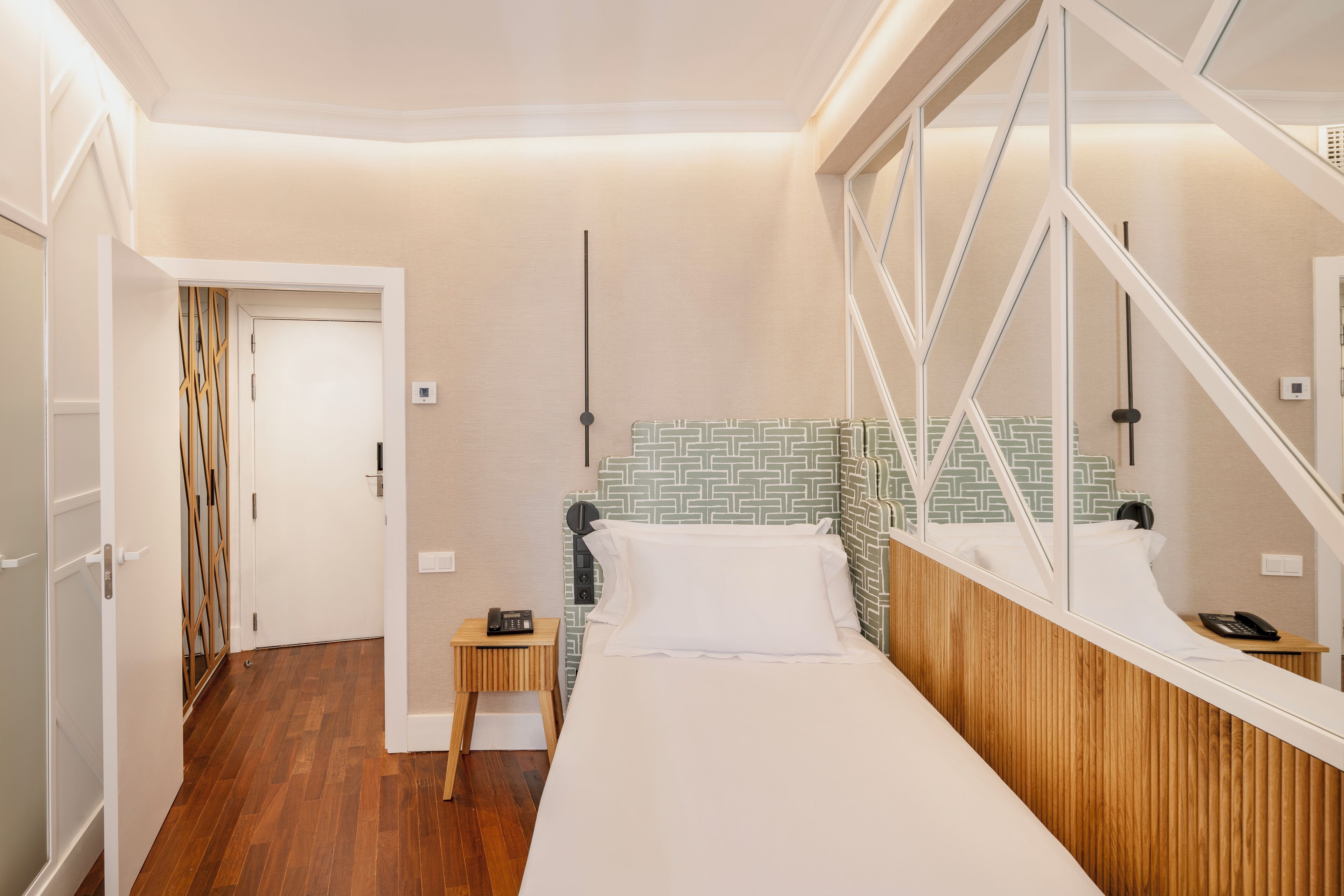 Una habitación de hotel con cama, mesita de noche, espejo y una puerta que da a otra habitación.