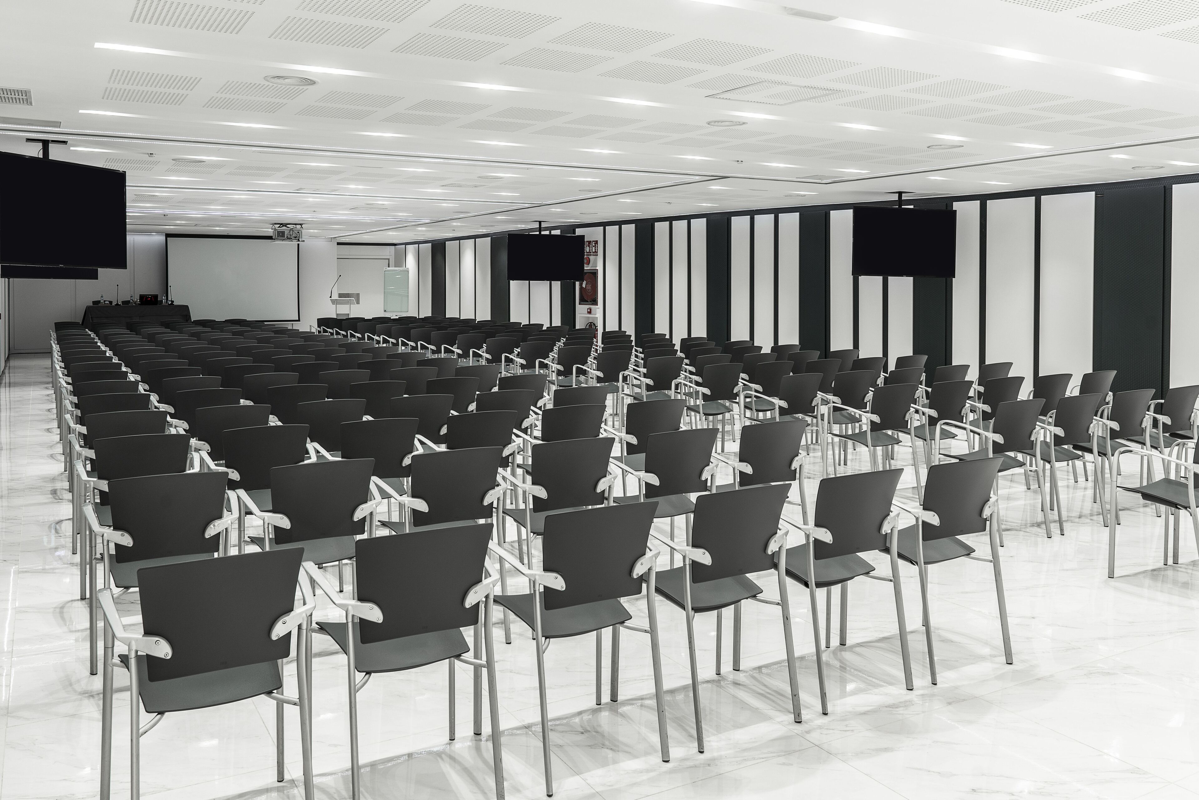 Una sala de conferencias con filas de sillas, una pantalla grande y un proyector.