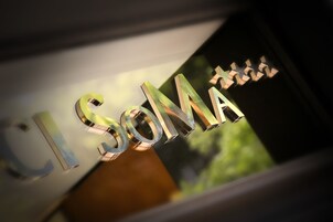 Un primo piano di un cartello metallico con le lettere "L'SOMA" e un simbolo a stella.