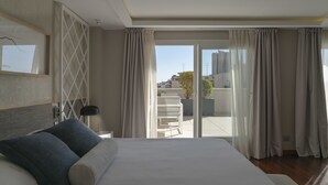 Et hotelværelse med en stor seng, et natbord, en skrivebordslampe og udsigt til den udvendige balkon.