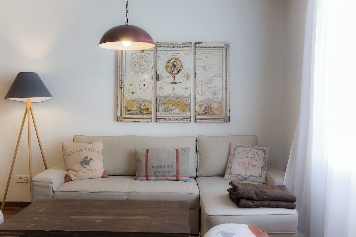 Una sala de estar acogedora con un sofá, una mesa de centro y una lámpara de pie. Hay almohadones decorativos en el sofá y un mapa mundial antiguo en la pared.