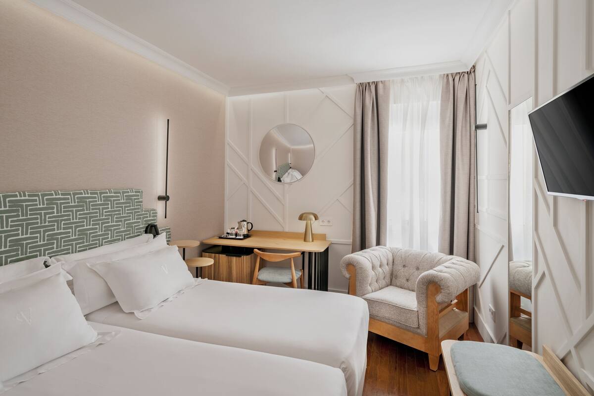 Habitación de hotel con dos camas, un escritorio, una silla, un televisor y un espejo.
