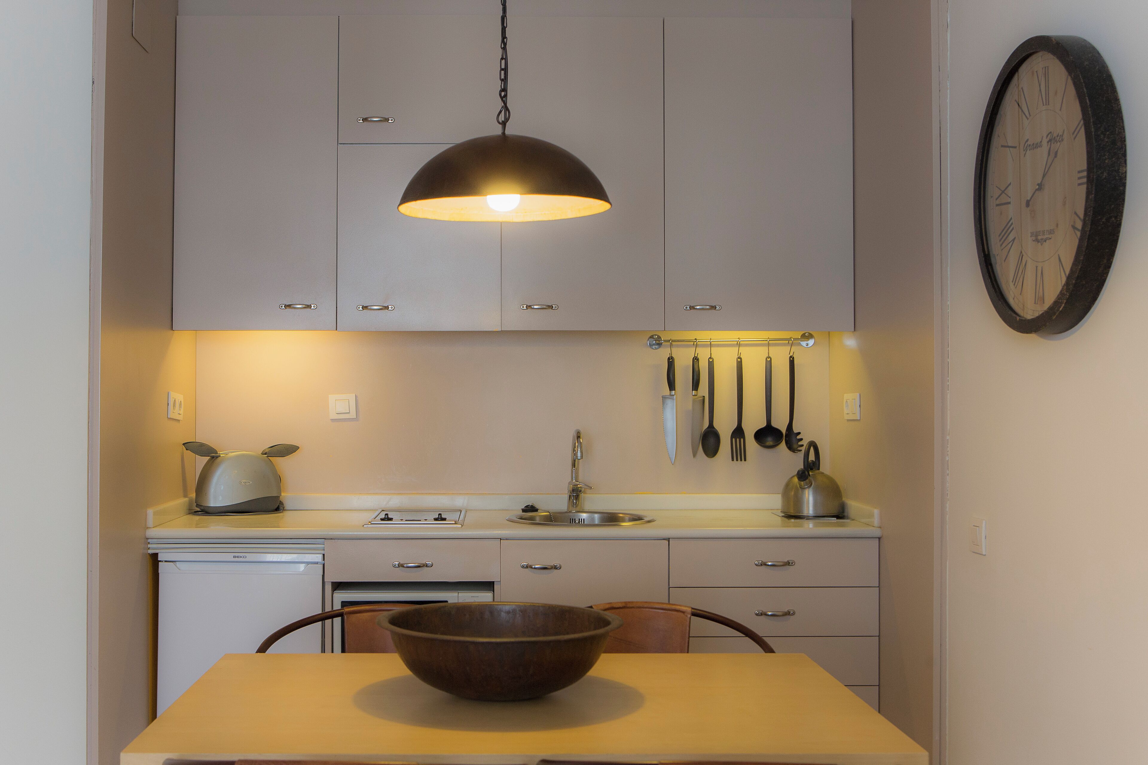 A kitchen with a wooden table, a hanging light fixture, and a wall-mounted clock.