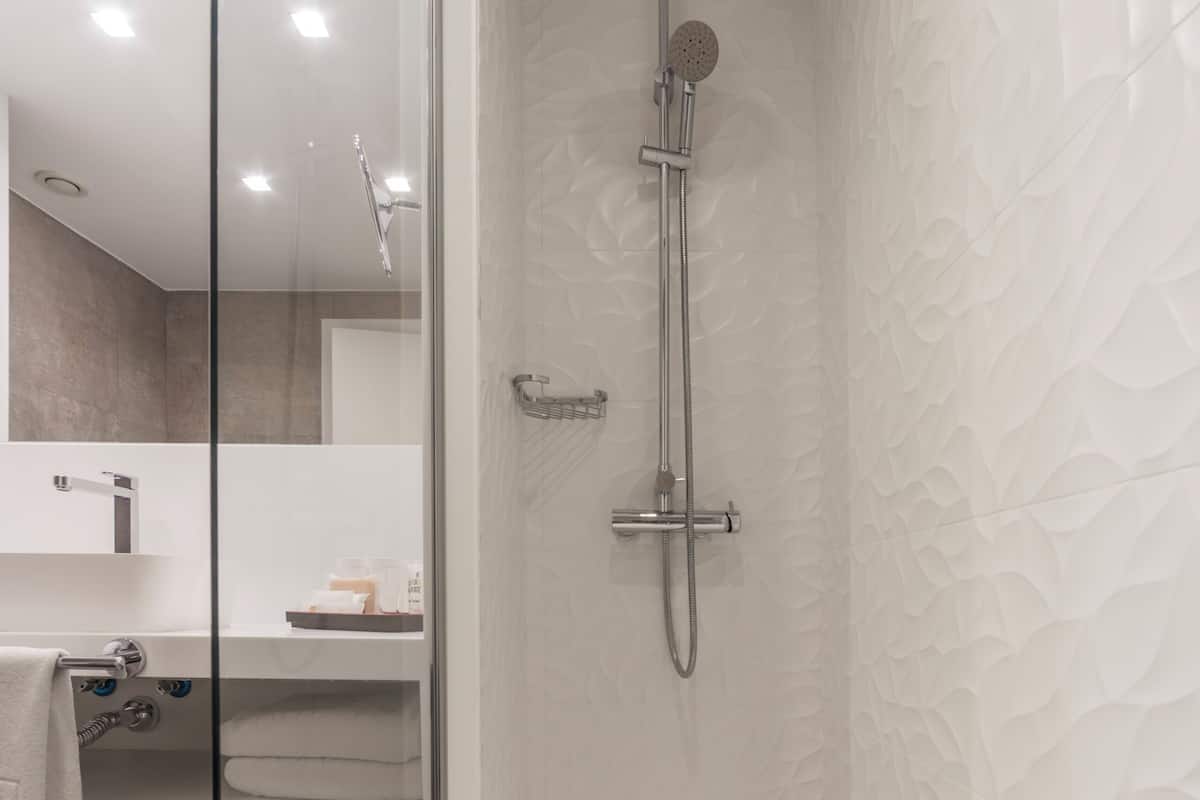Ein modernes Badezimmer mit Duschkabine aus Glas, einem weißen Waschbecken und einem sichtbaren Mülleimer.