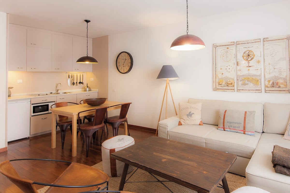 Un espacio habitable compacto con kitchenette, comedor y un sofá con cojines decorativos.