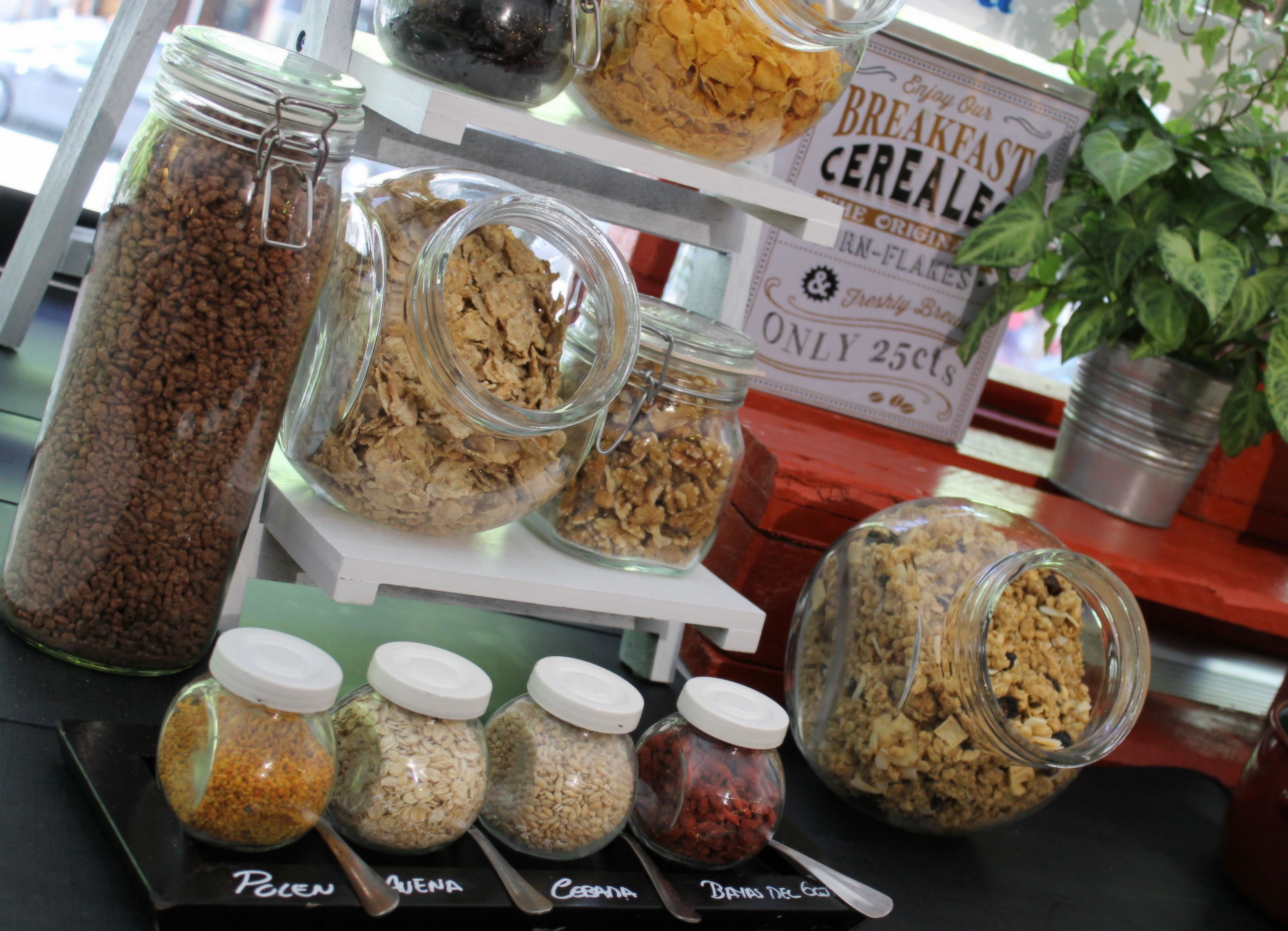 Una exhibición de diversos alimentos en frascos, como cereales y granos, sobre una mesa con un cartel sobre cereales para el desayuno.