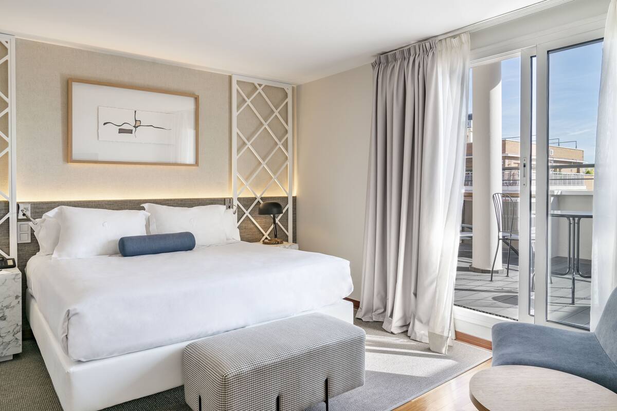Habitación de hotel con una cama grande, un sofá pequeño, un escritorio y vistas a la ciudad desde la ventana.
