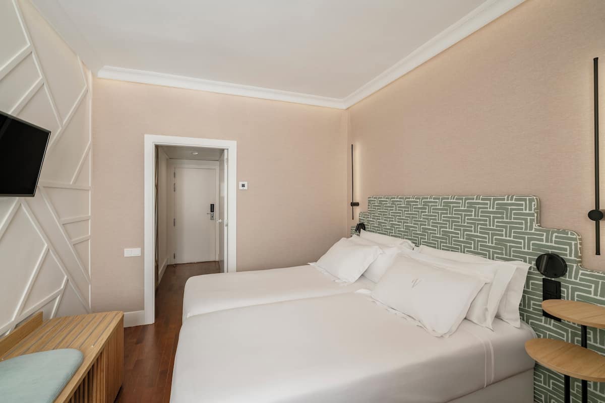 Habitación de hotel con cama, televisor, mesita de noche y una puerta que da a otra habitación.