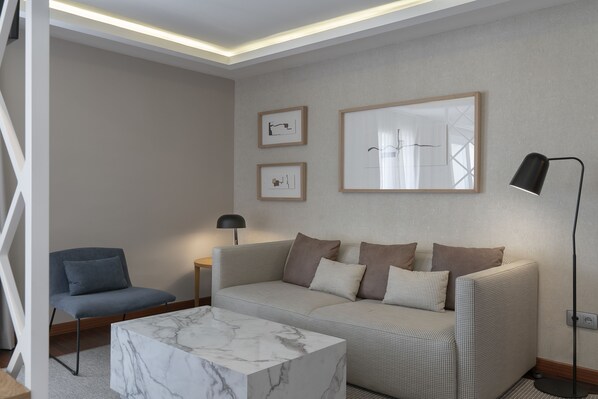 Una sala de estar moderna con un sofá, un sillón, una mesa de centro de mármol y obras de arte enmarcadas en la pared.