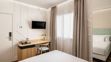 Une chambre d’hôtel comprenant un lit, un bureau avec une chaise, un téléviseur fixé au mur et une fenêtre avec des rideaux.