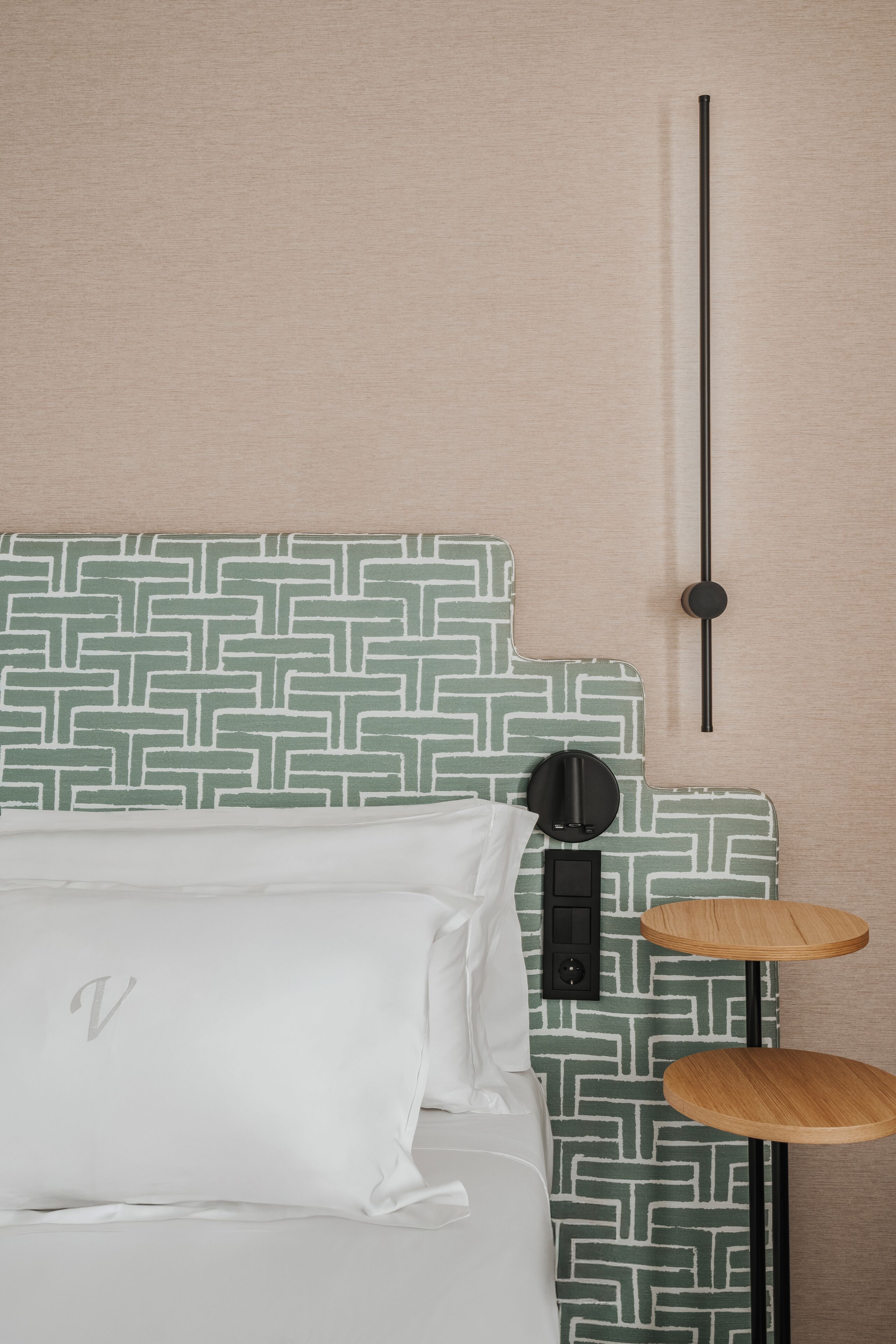 A bed with a patterned headboard, a bedside table, and a wall-mounted light fixture.