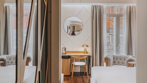Et hotelværelse med seng, skrivebord, stol, spejl og udsigt over byen.