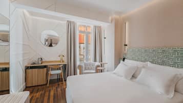 Habitación de hotel con una cama, un escritorio con silla, un espejo redondo y vistas a la ciudad desde la ventana.