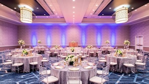 Une grande salle de banquet avec des tables rondes, des chaises et des centres de table floraux.