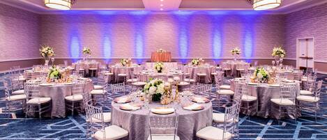 Un amplio salón de banquetes con mesas redondas, sillas y centros de mesa florales.